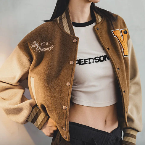 Person wearing a brown letterman jacket over a white crop top with visible branding.